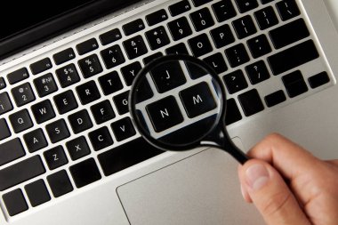 cropped shot of person holding magnifying glass above laptop keyboard clipart