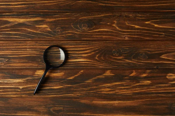 木製テーブルの上ハンドルを持つ単一の黒い虫眼鏡のトップ ビュー — ストック写真