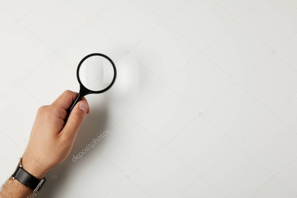 cropped shot of male hand with wristwatch holding magnifying glass on grey