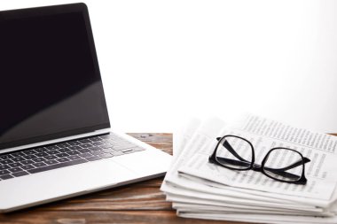 eyeglasses on newspapers and laptop with blank screen on wooden surface, on white clipart