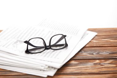 eyeglasses on pile of newspapers on wooden table, on white clipart