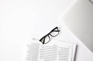 top view of eyeglasses, laptop and newspapers on white table clipart