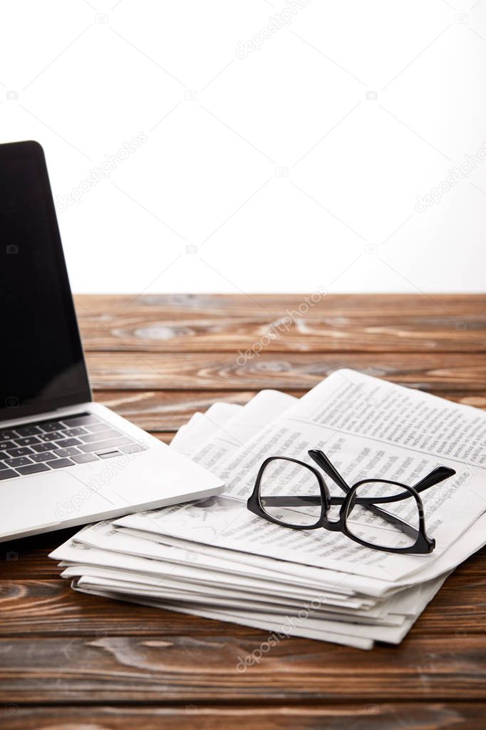 eyewear on pile of newspapers and laptop on wooden table, on white