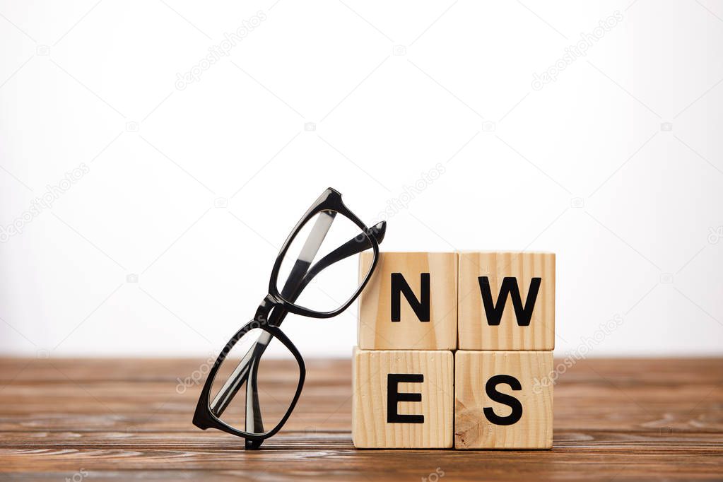 eyeglasses and alphabet cubes making word news on wooden surface, on white background