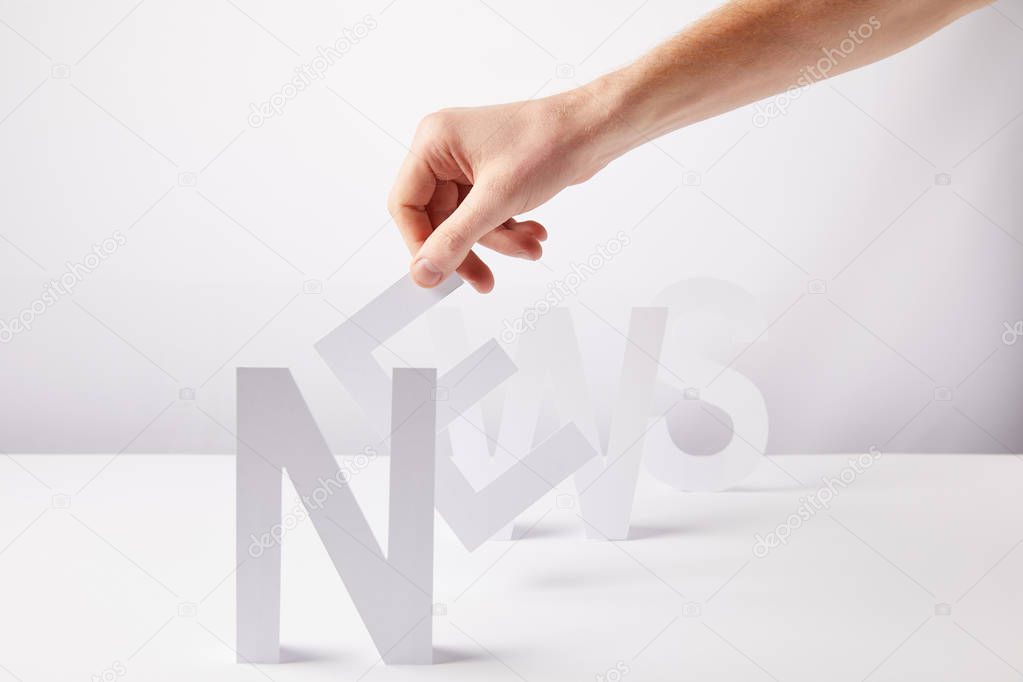 cropped view of person holding paper letters - word news, on white background