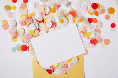 top view of confetti pieces, white paper and yellow envelope on white surface clipart
