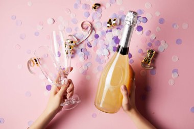 cropped image of woman holding bottle of champagne and glasses above confetti on party table clipart