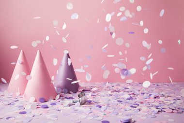 party hats under falling confetti pieces on violet tabletop clipart