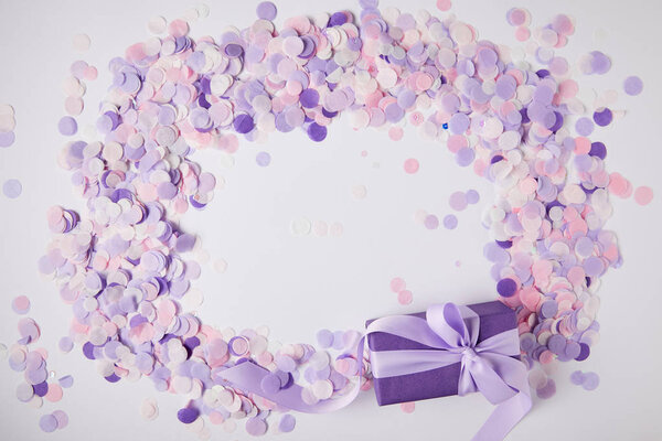 top view of gift box and violet confetti pieces on white surface
