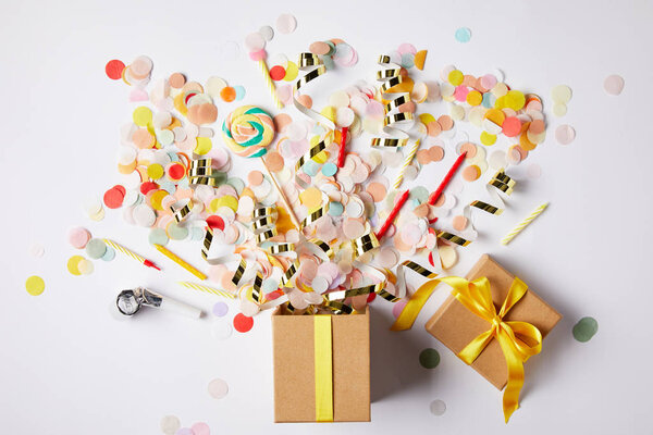 top view of gift box and scattered confetti pieces on white surface
