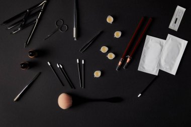 top view of brushes, pencils, cosmetics and tools for permanent makeup on black clipart