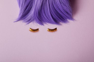 top view of bright violet wig and false golden eyelashes on purple