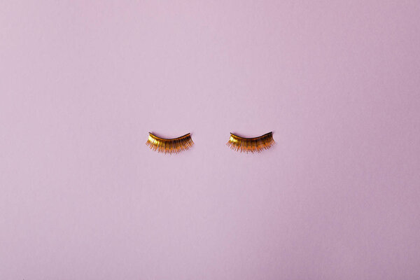 top view of stylish golden false eyelashes isolated on purple