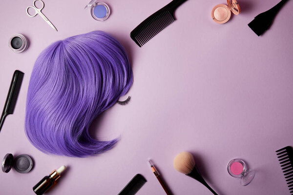 top view of violet wig, makeup tools and cosmetics on purple