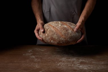 Erkek baker ekmek ahşap masa üzerinde tutarak önlük kadeh kırpılmış 