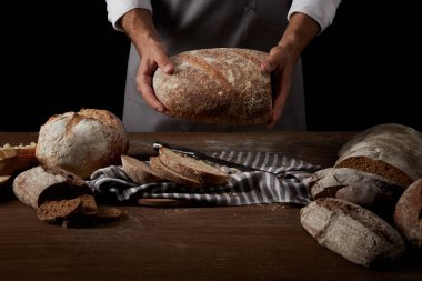 Erkek baker ekmek bıçağı, ekmek ve çul ile masa üzerinde tutarak önlük görüntü kırpılmış 