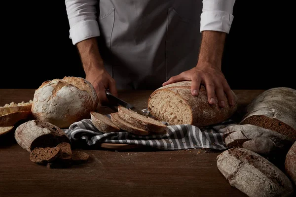 面包师在围裙上修剪面包的图片在木桌上的麻布上 — 图库照片
