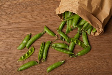 top view of pea pods spilled from paper bag on wooden table clipart