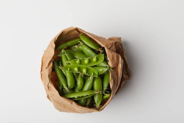 top view of ripe pea pods in paper bag on white surface clipart