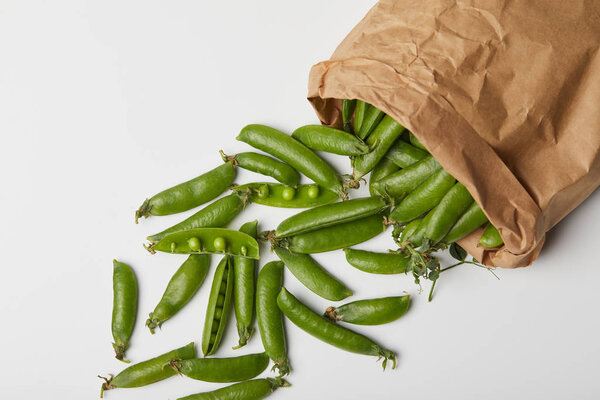 top view of pea pods spilled from paper bag on white surface