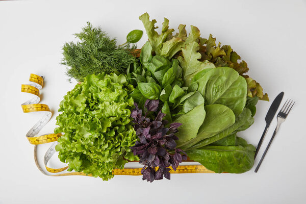 top view of various ripe vegetables in box with cutlery and measuring tape on white surface