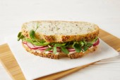close-up shot of sandwich with radish slices and green pea shoots on wooden cutting board