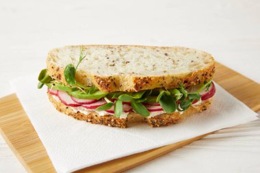 close-up shot of sandwich with radish slices and green pea shoots on wooden cutting board clipart