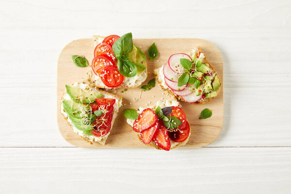 top view of delicious fresh sandwiches on cutting board on white wooden surface