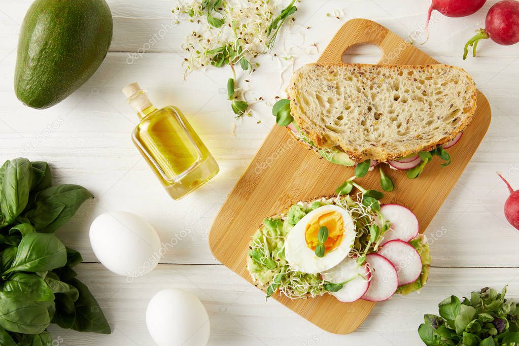 top view of sandwiches with eggs, avocado and radish on white wooden surface