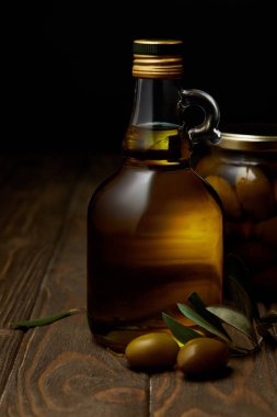 bottle of aromatic olive oil with branch and jar on wooden table clipart