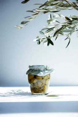jar of aromatic oil with green olives and branches on white table clipart