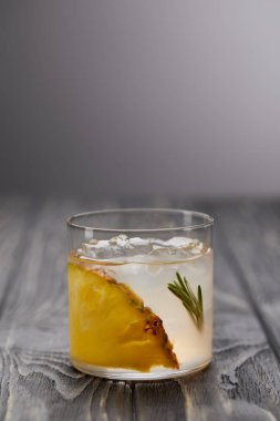 glass of lemonade with rosemary, ice cubes and pineapple on grey wooden table clipart