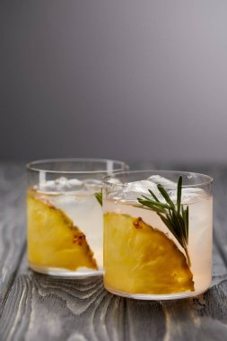 İki bardak limonata ananas parçaları, buz küpleri ve biberiye gri ahşap masa üzerinde