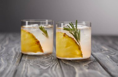 İki bardak limonata ananas parçaları, buz küpleri ve biberiye gri ahşap masa üzerinde