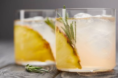 İki bardak limonata ananas parçaları, buz küpleri ve biberiye gri ahşap masa üzerinde seçici odak