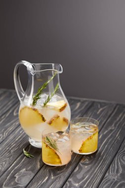 sürahi ve iki bardak limonata ananas parçaları, buz küpleri ve biberiye gri ahşap masa üzerinde