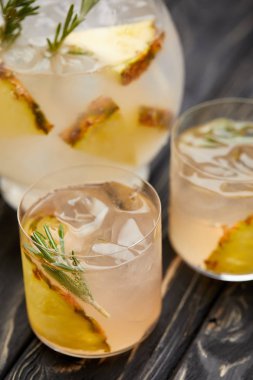 sürahi ve iki bardak limonata ananas parçaları, buz küpleri ve biberiye ile kısmi görünümü gri ahşap masa üzerinde