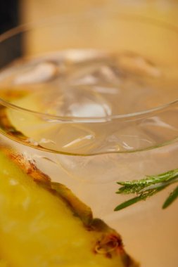 selective focus of glass of lemonade with ice cubes, pineapple pieces and rosemary clipart