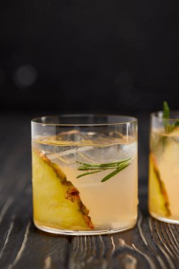 partial view of two glasses of lemonade with pineapple pieces, ice cubes and rosemary on grey wooden tabletop clipart