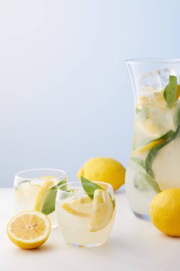 sürahi ve iki bardak limonata nane yaprakları, buz küpleri ve mavi zemin üzerine limon dilimleri ile 