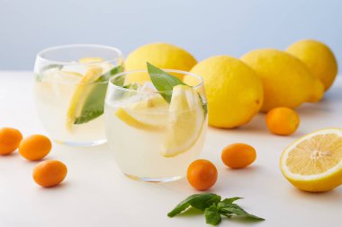 İki bardak limonata nane yaprakları, buz küpleri ile kumquats ve limon mavi zemin üzerine çevrili limon dilimleri 