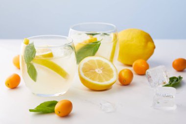 İki bardak limonata nane yaprakları, buz küpleri ile kumquats ve limon mavi zemin üzerine çevrili limon dilimleri 