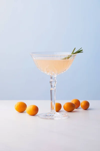 蓝色背景下的金橘围绕着迷迭香的酒杯鸡尾酒 — 图库照片