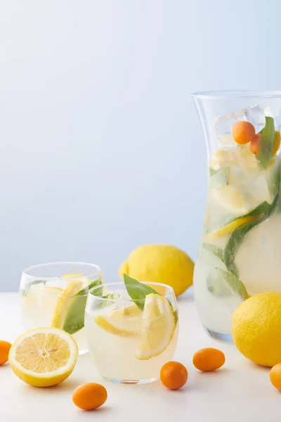 壶和两杯柠檬水与薄荷叶 冰块和柠檬片周围的金橘和柠檬在蓝色背景下 — 图库照片