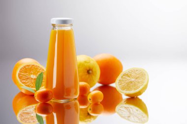 bottle of fresh juice with oranges, lemons and kumquats on reflective surface clipart
