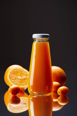 bottle of fresh orange juice with oranges and kumquats on reflective surface isolated on black clipart