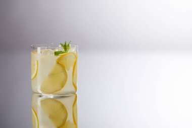 single glass of fresh lemonade on reflective surface and on grey clipart
