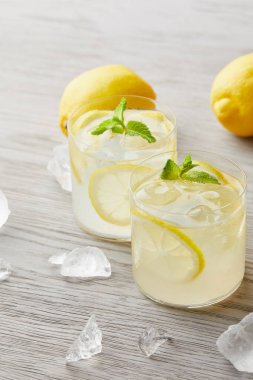 glasses of delicious lemonade with ice and lemons on wooden surface clipart