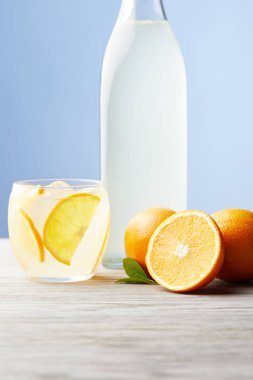 Cam ve ahşap masa üzerinde olgunlaşmış portakal ile turuncu limonata şişe