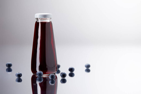 glass bottle of fresh blueberry juice on reflective surface